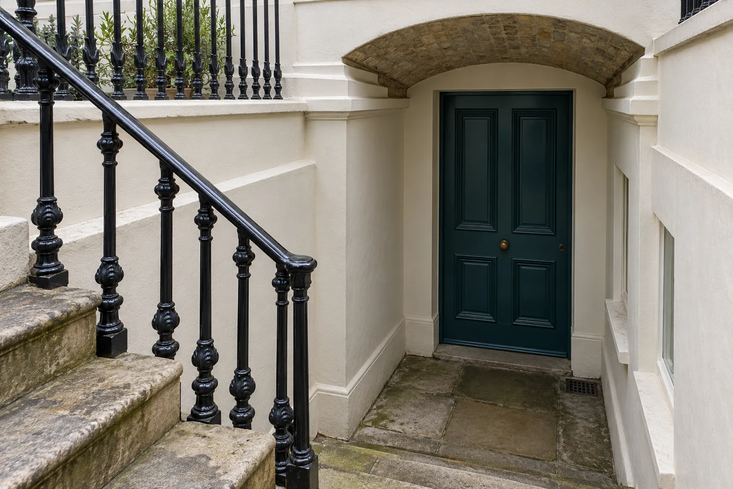 Black railings and stone steps descending to a painted basement entrance beneath a shallow vault